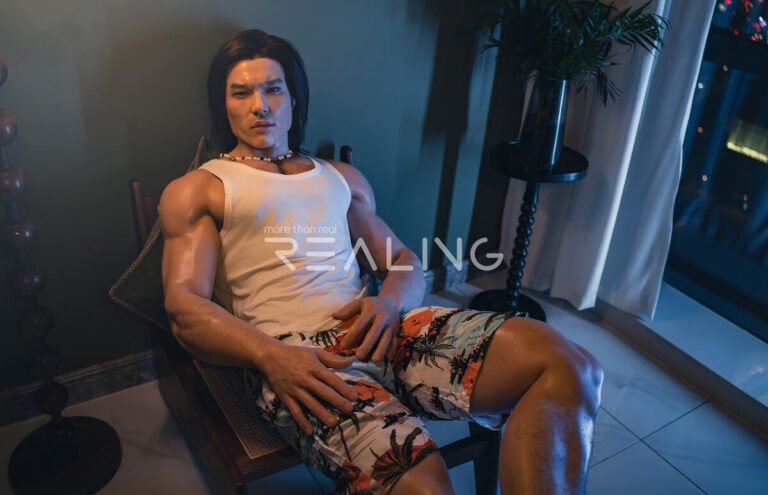 gay man sitting alone at laptop with male doll beside him